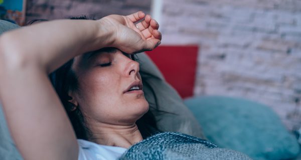 Sick young woman lying in the bed covered with blanket. Ill woman lying in bed with high temperature.