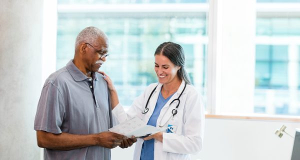 A mid adult female doctor places her hand on a senior male patient's shoulder as she discusses home care options with him.