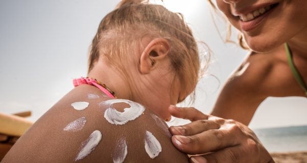 Close up of a mother applying moisturizer on her daughter's shoulder while spending a summer day on the beach.