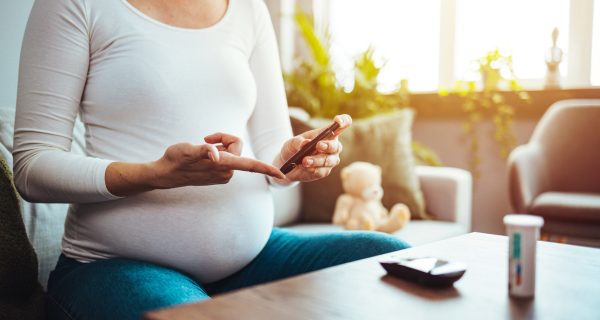 Happy Pregnant woman with glucometer checking blood sugar level at home. Woman testing for high blood sugar. Pregnant Woman holding device for measuring blood sugar.